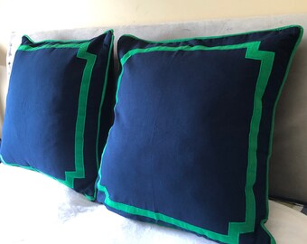 May include: Two navy blue throw pillows with green trim. The pillows have a square shape and a simple design.
