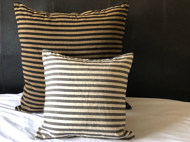 May include: Two striped throw pillows, one with black and tan stripes and one with black and white stripes, on a white bed.