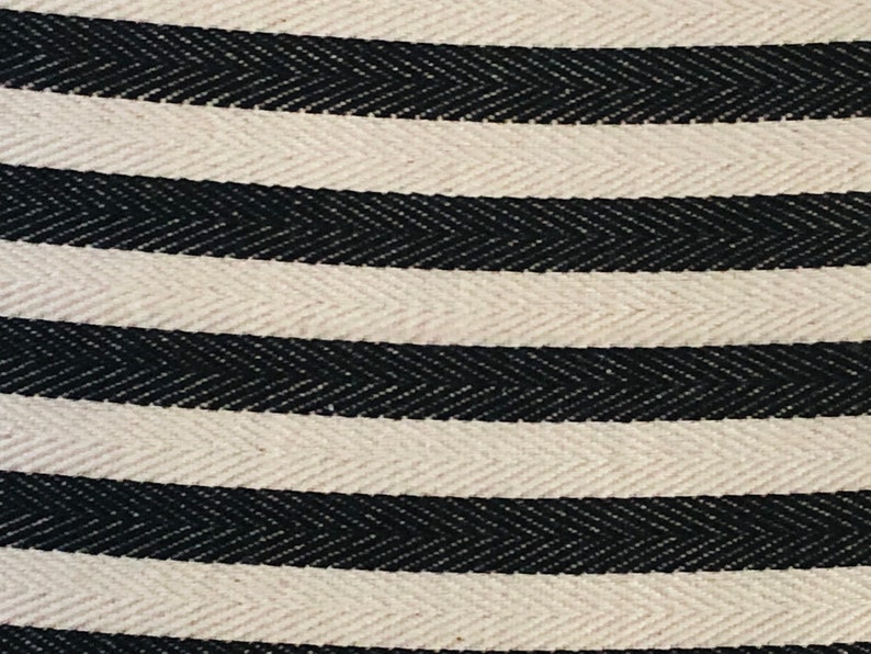 May include: Close-up of a white and black striped fabric with a herringbone pattern. The fabric is woven with a subtle texture.
