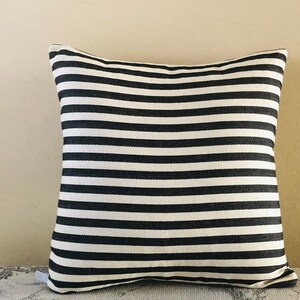 May include: Black and white striped throw pillow with a simple design. The pillow is made of a soft, woven fabric.