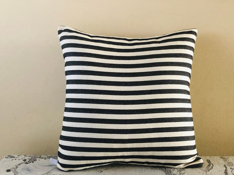 May include: Black and white striped throw pillow with a simple design. The pillow is made of a soft, woven fabric.