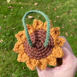 May include: A crocheted sunflower with a brown centre and orange petals. The sunflower has a green stem.