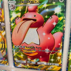 May include: Lickilicky ex Pokemon card with a pink and white Lickilicky illustration. The card has a gold background with stars and a green border. The card text reads "Licking Fury 100+" and "Flip a coin until you get tails. This attack does 40 more damage for each heads."