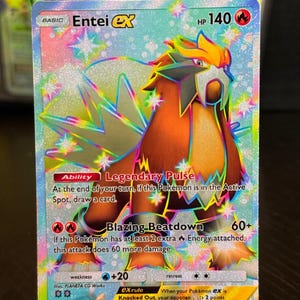 Könnte beinhalten: Eine holografische Entei EX Pokémon-Sammelkarte. Die Karte zeigt eine detaillierte Illustration von Entei, einer feurigen, löwenartigen Kreatur, mit einem braunen, orangefarbenen und weißen Farbschema. Die Karte enthält Text, darunter "Legendary Pulse" und "Blazing Beatdown".