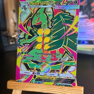 Op de afbeelding: Een Mega Sceptile EX ruilkaart met een holografische afwerking, met een illustratie van een groen wezen, 210 HP en de aanval Terminating Tail. De kaart bevat tekst waaronder Mega Sceptile EX, 130 schade en de Mega Evolution EX-regel.