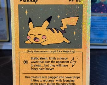 May include: A holographic Pokémon trading card featuring "Pikanap." The card shows a sleeping yellow Pikachu with black ears and a lightning bolt tail. The card has text that reads "HP 60" and "9/50."