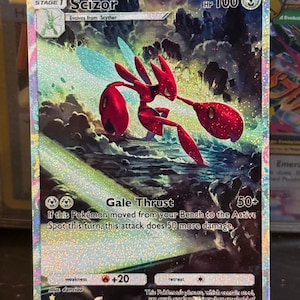 May include: A holographic Scizor Pokémon card. The card features a red insectoid creature with large pincers and wings, set against a dynamic, colorful background. Text includes "Scizor", "Gale Thrust", and "HP 100".