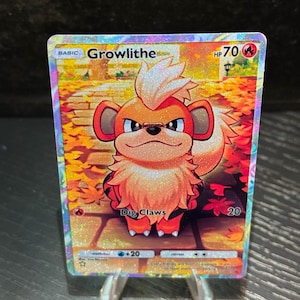 Puede incluir: Una tarjeta coleccionable holográfica de Pokémon Growlithe. La tarjeta presenta un personaje Growlithe naranja y blanco con el texto "Dig Claws". La tarjeta se muestra en un soporte de plástico transparente.
