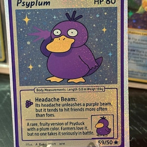 May include: A holographic Psyplum Pokémon card with a purple duck-like creature. The card has the text "Psyplum" and "HP 80". The card also includes the text "Headache Beam" and "59/50". The card is held in a clear plastic stand.