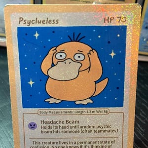 May include: A holographic trading card with a cartoon Psyduck character, hands on its head, against a blue starry backdrop. The card reads "Psyclueless" and "HP 70". The card also includes the text "Headache Beam". The character's length is 1.2 m.