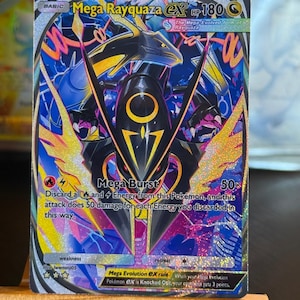 Peut inclure: Une carte à collectionner holographique Mega Rayquaza EX représentant une créature noire semblable à un dragon avec des accents jaunes. La carte affiche le texte Mega Rayquaza EX, HP 180 et Mega Burst 50x, sur un fond abstrait bleu, rose et jaune.