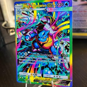 Puede incluir: Una tarjeta Pokémon Mega Blastoise EX holográfica. La tarjeta presenta una vibrante ilustración de Blastoise en tonos azules, amarillos y rosas, con el texto "Triple Bombardment 130". La tarjeta se muestra en un soporte transparente.