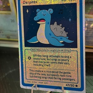 May include: A holographic trading card featuring a blue cartoon creature named Derpras with the text "HP 100". The card includes the text "Off-Key Song" and "Body Measurements: Length 2.5 m Wt 220 kg". The card is numbered 47/50.