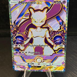 May include: A holographic Mewtwo EX Pokémon trading card. The card features a white and purple Mewtwo character with the text "Psychic Sphere" and "Psydrive". The card is displayed on a clear acrylic stand.