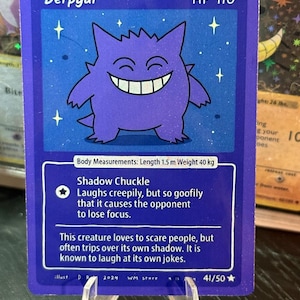 May include: A purple "Derpgar" trading card featuring a smiling cartoon character, HP 110. The card details the character's abilities and measurements: 1.5 m length, 40 kg weight. The card is part of a 41/50 set.