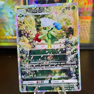 May include: A holographic Pokémon trading card featuring Roserade. The card has a green and white floral design with a character illustration. The card text includes "Roserade", "Poison Ring", and "HP 90".