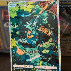 May include: A holographic trading card featuring the Pokémon Totodile. The card depicts Totodile in a watery environment, with the text "Wave Splash" and other game-related details. The card has a basic design with a HP of 60.