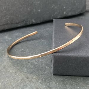 May include: A thin gold hammered bangle bracelet. The bracelet is simple and delicate, with a smooth, polished finish.