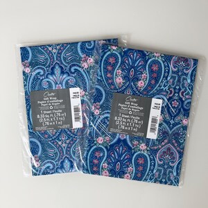 May include: Two sheets of Carlton Cards gift wrap in clear plastic sleeves. The paper features a blue paisley pattern with pink floral accents. Each label states 1 sheet, 8.33 sq. ft. (.76 m2), and dimensions of 0.76 m x 1 m (2.5 ft. x 1.1 yd.).