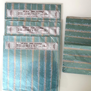 May include: Three sealed packages and one loose sheet of teal gift wrap featuring a pattern of vertical stripes in light blue, white, and gold. Each package label states 2 Sheets, 50.2 x 73.7 cm, and All Occasion General.