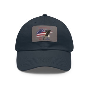 Könnte beinhalten: Eine marineblaue Baseballkappe mit einem Aufnäher, der einen amerikanischen Weißkopfseeadler zeigt, der über einer amerikanischen Flagge mit dem Text "My Freedom Ain't Free" und "U.S.A." fliegt.