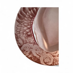 May include: A light pink hat featuring a wide brim decorated with a detailed dark red print of layered feathers and blooming roses. The crown of the hat is smooth and solid light pink, contrasting with the intricate floral and wing pattern.