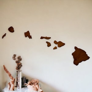 May include: A set of dark brown wooden wall art pieces shaped like the individual islands of Hawaii. The cutouts are arranged horizontally to represent the geographic layout of the archipelago, featuring smooth edges and a natural wood grain finish.