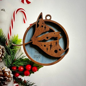 May include: A wooden Christmas ornament with a blue background and a brown cutout of a stylized butterfly. The ornament is inscribed with the text "Mar 2022".