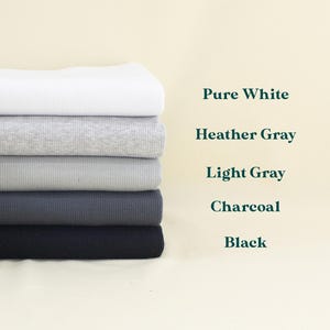 A stack of six different colored fabrics, including pure white, Heather Gray, Light Gray, Charcoal, and Black, arranged in a row against a light background.
