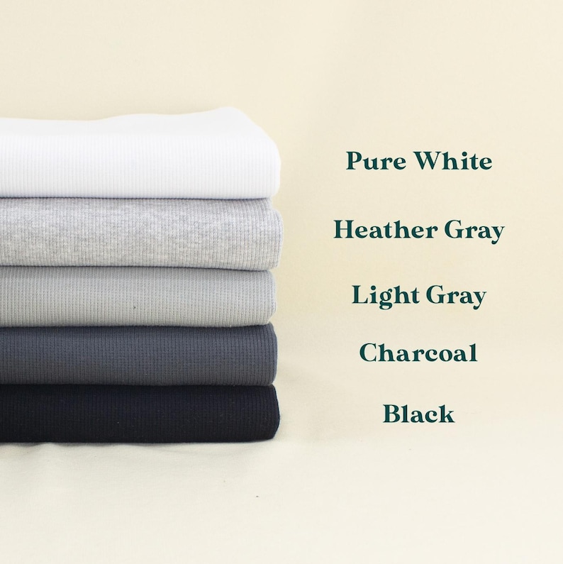 A stack of six different colored fabrics, including pure white, Heather Gray, Light Gray, Charcoal, and Black, arranged in a row against a light background.