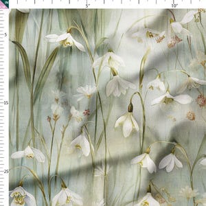 May include: A fabric featuring a watercolour floral pattern. White snowdrop flowers with yellow centres and green stems are set against a pale green backdrop. The design includes long green leaves and small, delicate flowers.