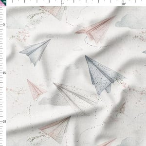May include: Fabric with a watercolour design of paper aeroplanes in pink and blue on a white backdrop. The pattern includes delicate cloud and floral details, giving a whimsical, light feel. Suitable for children's crafts and projects.