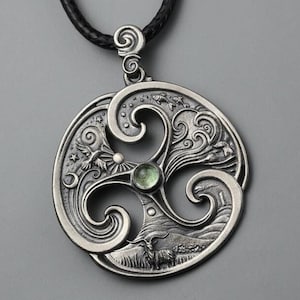 May include: Silver pendant necklace with a green gemstone in the center of a circular design. The design features three swirling spirals with a detailed scene of a landscape, birds, and a sun.