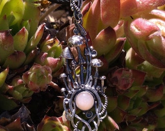 May include: A silver pendant necklace with a mushroom design and a pink opal stone in the center. The pendant is hanging from a black cord.