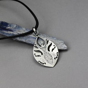 May include: A silver pendant necklace with a detailed design of a woman standing in a leaf shape. The pendant is on a black cord.