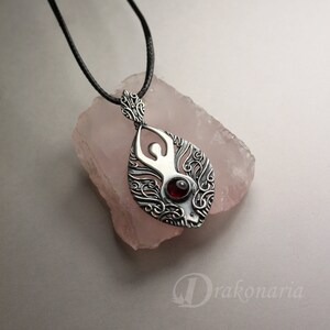 May include: A silver pendant necklace with a detailed design of a woman's figure with a red gemstone in the center. The pendant is hanging on a black cord.