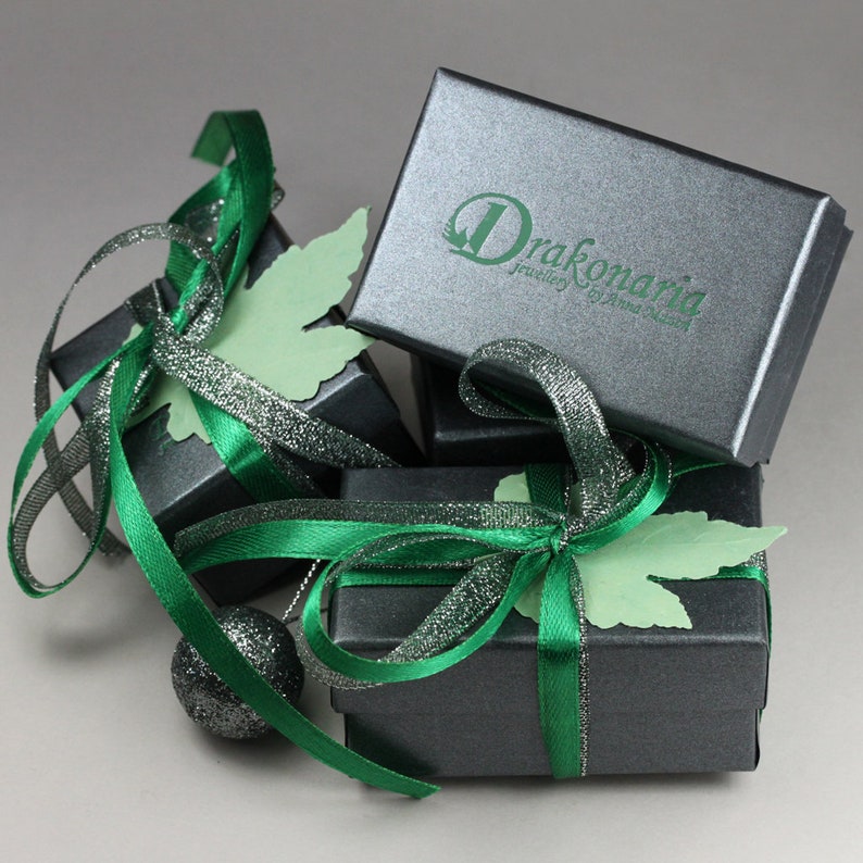 May include: Three small, dark gray gift boxes with green ribbon and a green leaf design. The top box has the text "Drakonaria Jewellery by Anna Sakala" printed on it.