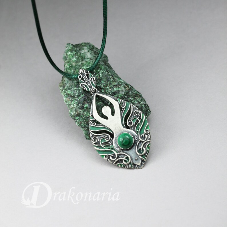 May include: A silver pendant necklace with a green malachite stone in the center. The pendant features a stylized human figure surrounded by intricate floral designs.
