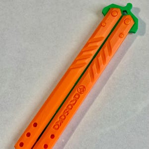 May include: Orange and green plastic butterfly knife with the word "DROPS" printed on the handle.