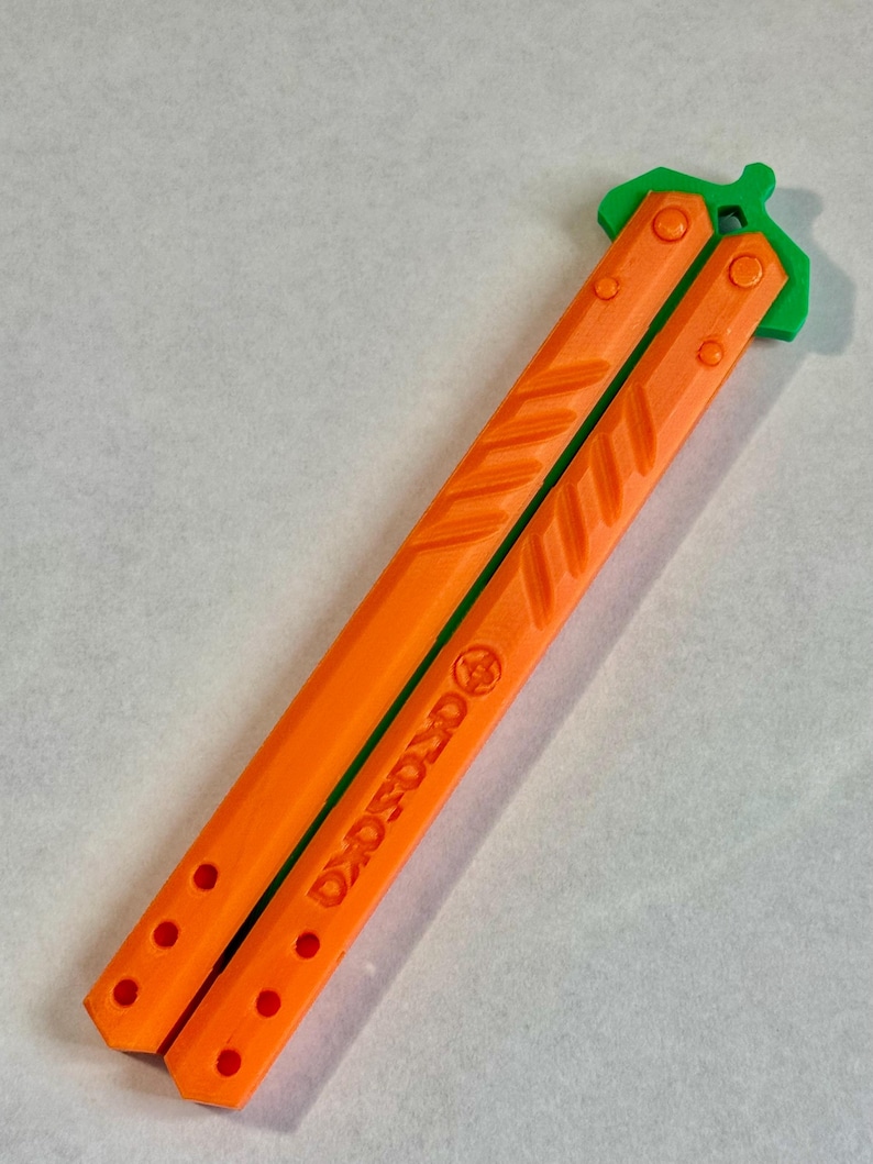 May include: Orange and green plastic butterfly knife with the word "DROPS" printed on the handle.