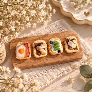 Könnte beinhalten: Vier Miniatur-Toastscheiben auf einem rechteckigen Holzbrett. Die erste Scheibe ist mit einem Spiegelei und Speck belegt, die zweite mit Schokoladenaufstrich und Marshmallows, die dritte mit weißer Creme, Kiwi und Blaubeeren und die vierte mit Schokoladenaufstrich und Bananenscheiben.
