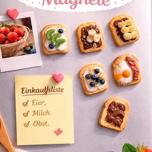 Może przedstawiać: Kolekcja magnesów w kształcie mini tostów z różnymi dodatkami, takimi jak owoce, czekolada i jajka. Żółta karteczka z napisem Einkaufsliste, Eier, Milch, Obst jest przymocowana różowym magnesem w kształcie serca. Widoczne jest także zdjęcie truskawek.