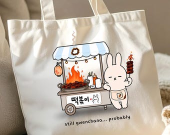 Puede incluir: Un bolso de tela color crema con un gráfico de un conejo blanco junto a un puesto de comida con fuego, una sartén con comida y texto en coreano. Debajo del puesto, el texto dice, still gwenchana... probably, en letras minúsculas negras.