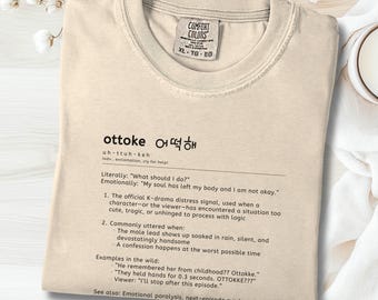Puede incluir: Camiseta marfil Comfort Colors con la palabra "ottoke" en negro y su definición en inglés y coreano. La camiseta tiene cuello redondo y mangas cortas. Talla XL-TG-EG.