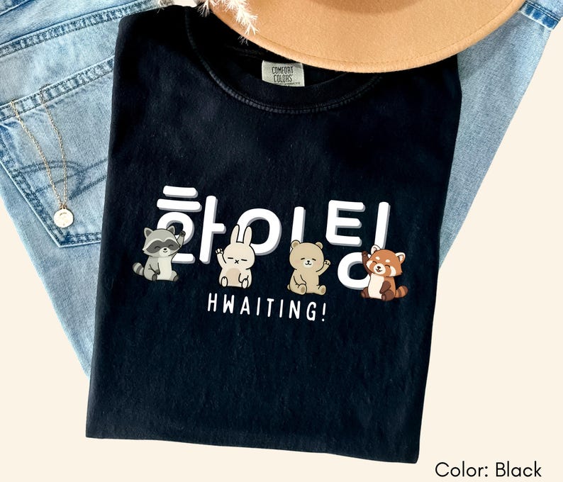 May include: Black t-shirt with the Korean word "Hwaiting" and the English word "Hwaiting!" below, along with cartoon raccoon, rabbit, bear, and red panda graphics. The shirt is folded on top of blue jeans.