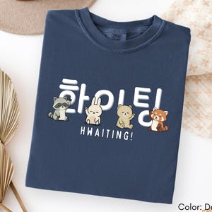 May include: Denim blue t-shirt with a graphic featuring cartoon animals and Korean characters. The text "HWAITING!" is printed below the animals. The shirt is a Comfort Colors brand.