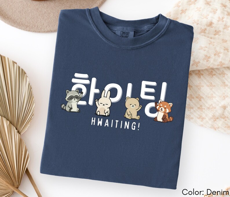 May include: Denim blue t-shirt with a graphic featuring cartoon animals and Korean characters. The text "HWAITING!" is printed below the animals. The shirt is a Comfort Colors brand.