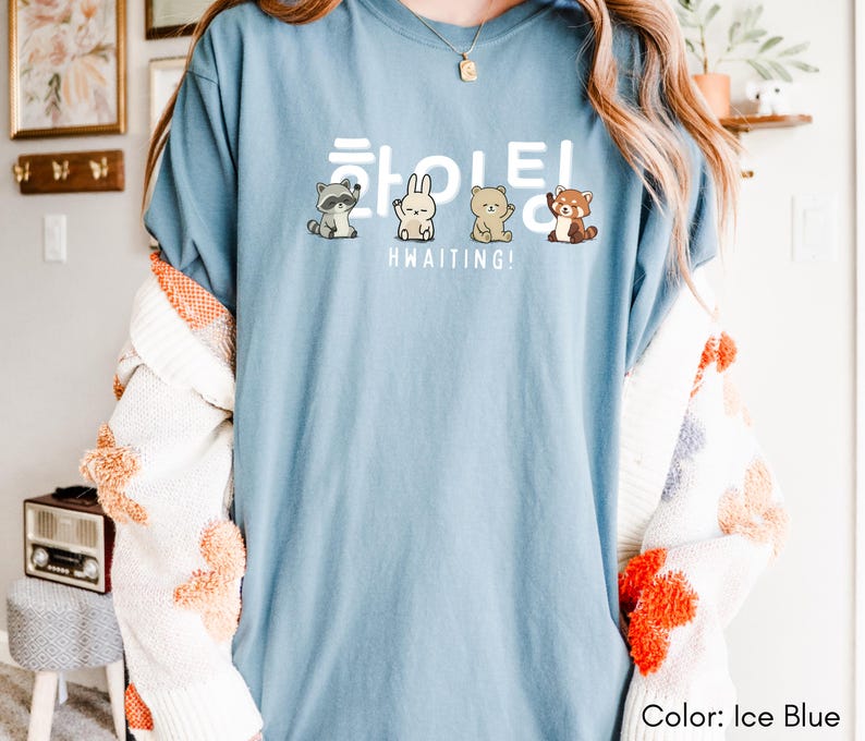 May include: Ice blue t-shirt with the word "Hwaiting!" in white Korean characters and English text. The shirt features cartoon illustrations of a raccoon, rabbit, bear, and red panda. The shirt is a light blue color.