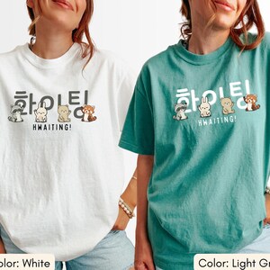 May include: White and light green t-shirts with a graphic design. The design features Korean text and cartoon animals. The text reads "Hwaiting!" and "Hwaiting!" in English. The t-shirts are casual wear.