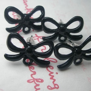 Peut inclure: Quatre paires de boucles d'oreilles à clous en forme de nœud papillon noir. Chaque boucle d'oreille présente un design de nœud noir brillant et uni avec une boucle en bas. Les boucles d'oreilles sont montées sur des tiges transparentes.